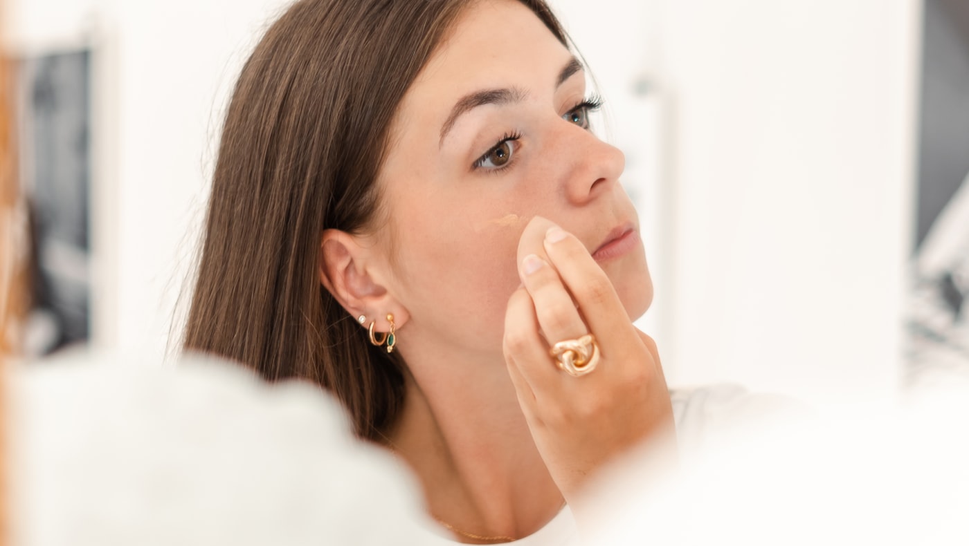 Woman applying a luxury face cream at a bathroom mirror in natural daylight