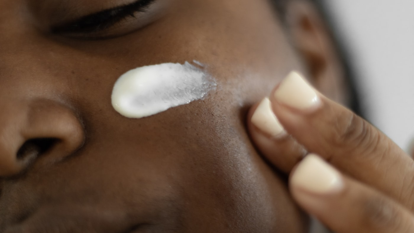 Close-up of a woman applying a white moisturiser to her cheek