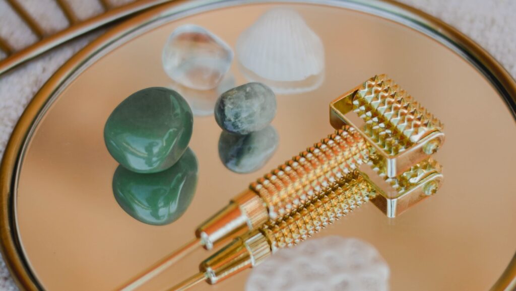 Gua sha stones and a gold facial roller arranged on a mirrored tray in warm light