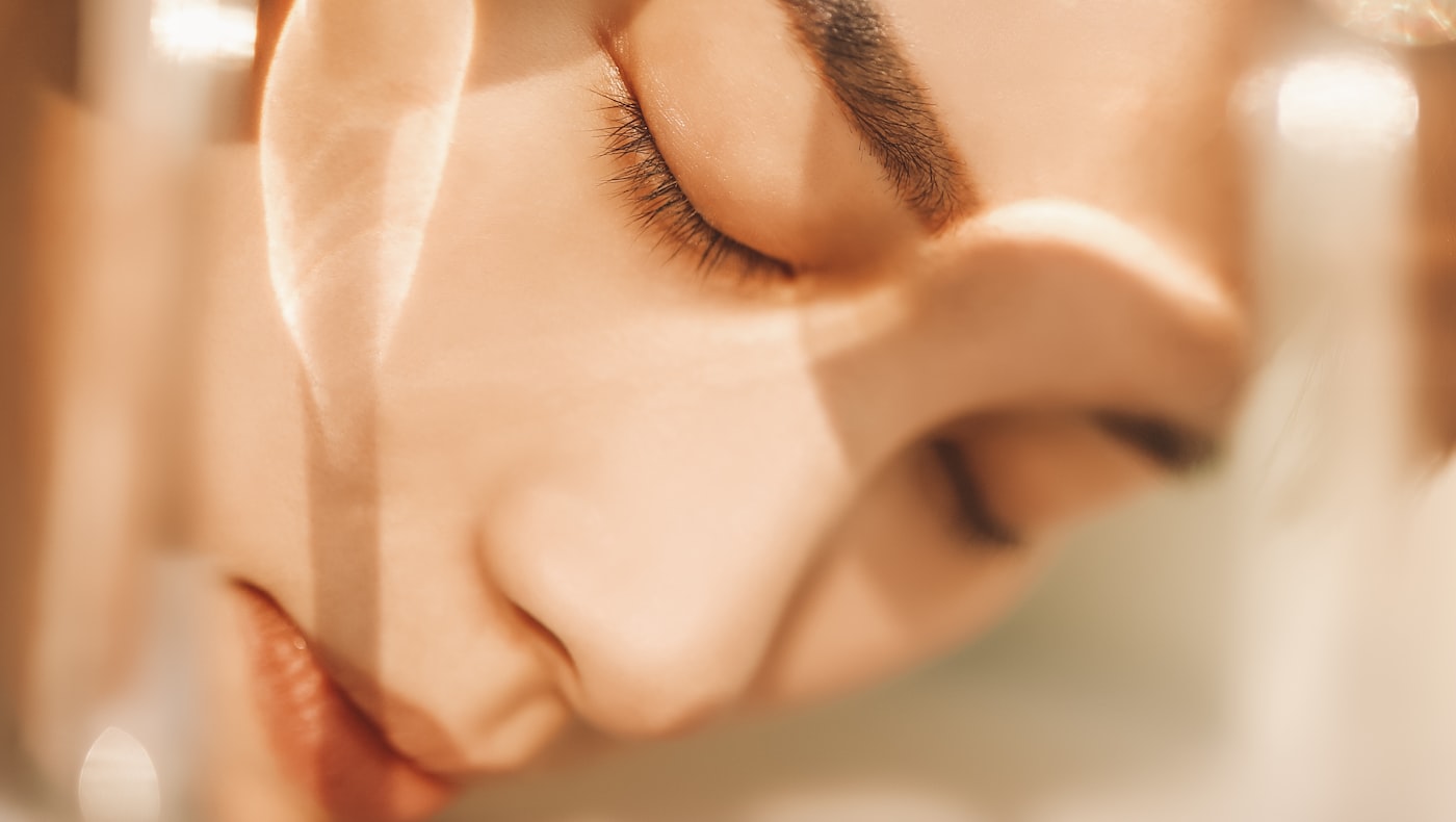 Woman with eyes closed in warm evening light during her nighttime skincare routine