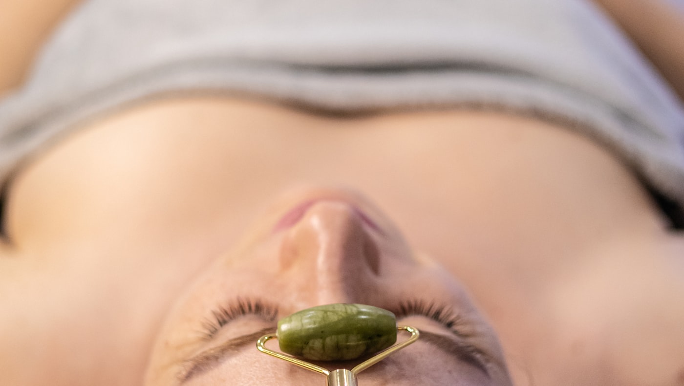 Close-up of a woman having a facial massage with a jade roller in soft light