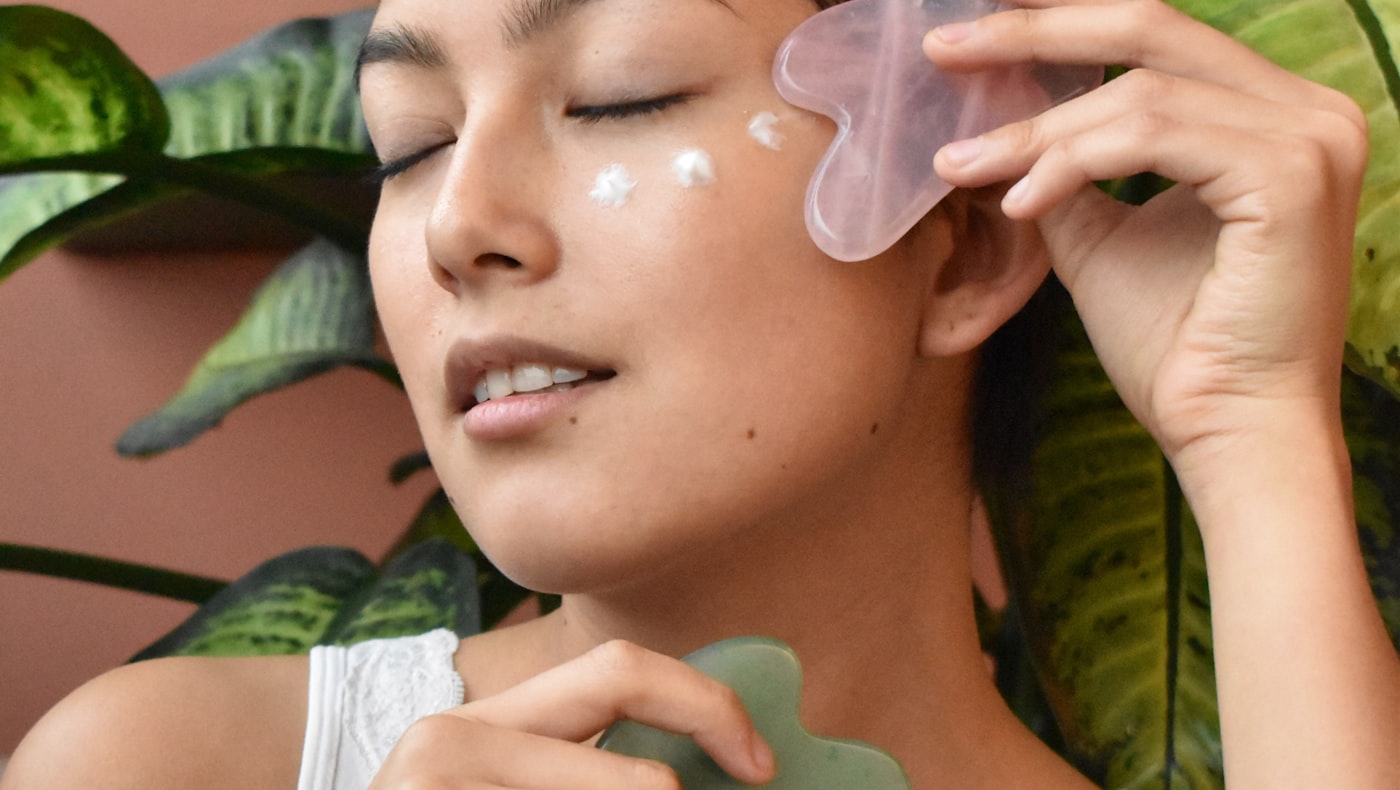 Woman with eyes closed using a rose quartz gua sha tool on her cheek