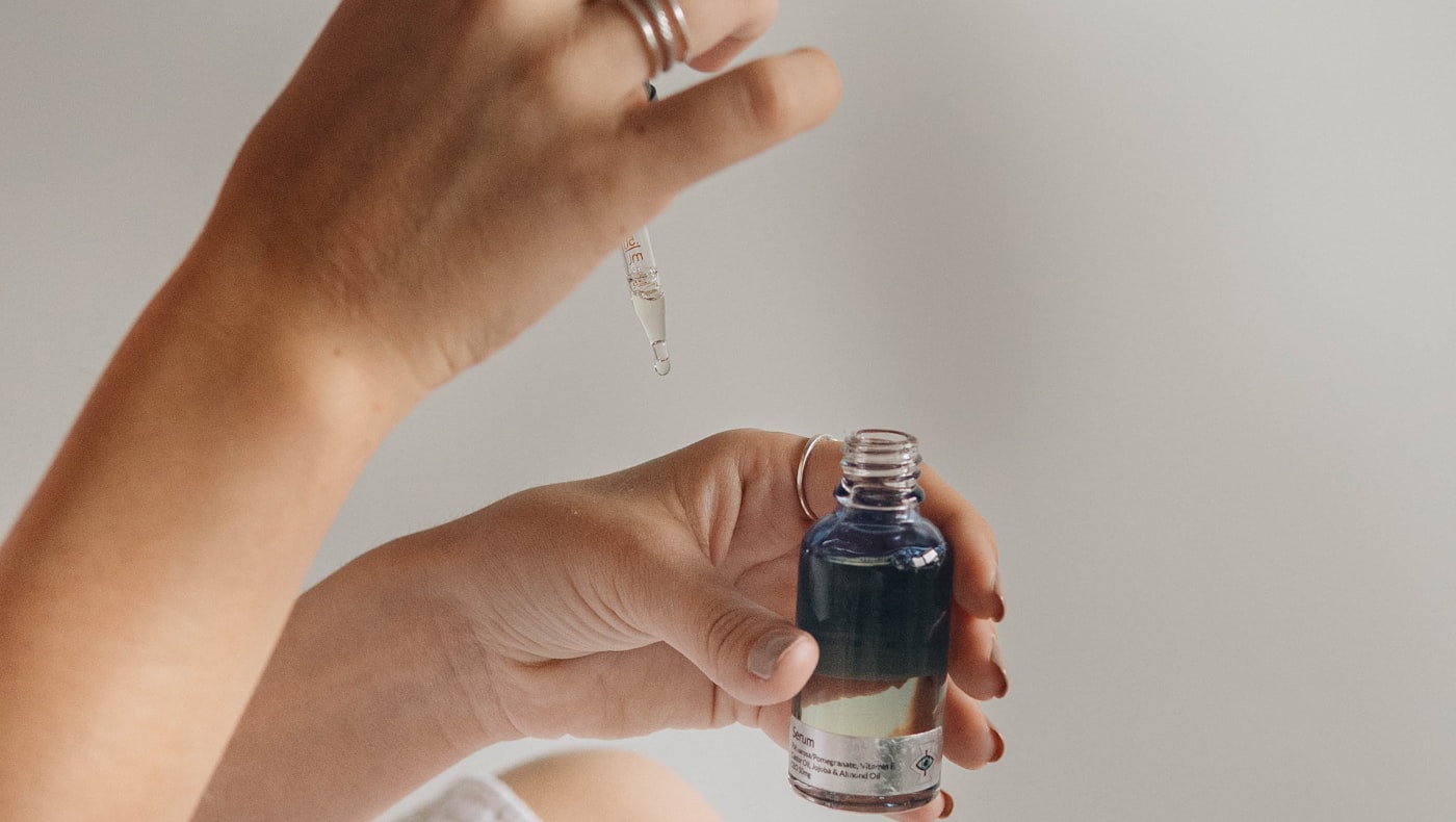 Hands holding a glass serum bottle and reading its ingredient list